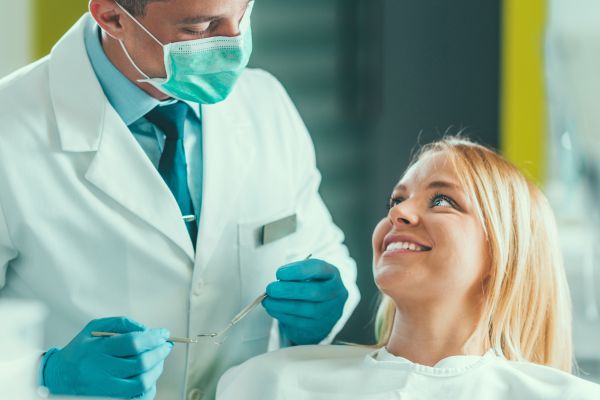 A dentist is standing next to his dental patient, who is sitting in the treatment chair awaiting treatment.