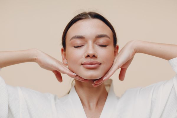 Dermal Fillers in Newport - Photo of a woman with her head resting on the top of her hands. She has her eyes closed and is smiling. She is wearing a white shirt.