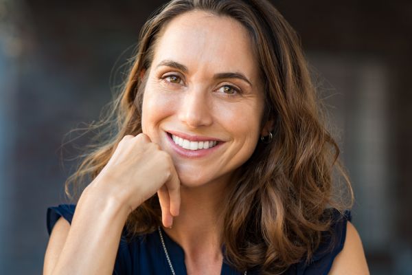 Close-up photo of a woman with shoulder-length brown hair resting her chin on her right hand and smiling