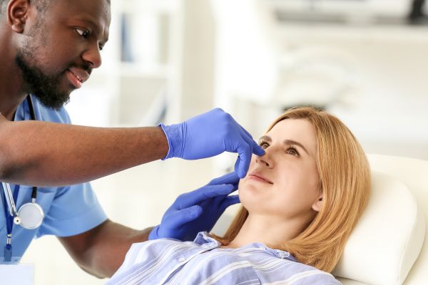 Photo of a male dental consultant examining the nose of a female patient.