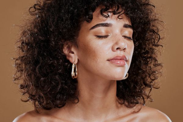 Photo of a woman with long curly black hair. Her head is facing towards her left shoulder and she has her eyes shut.