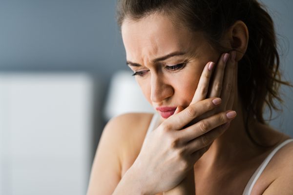 Wycherleys Dental Practice - About Us Page - photo of a woman holding her left cheek with both hands. She looks like she has a toothache.