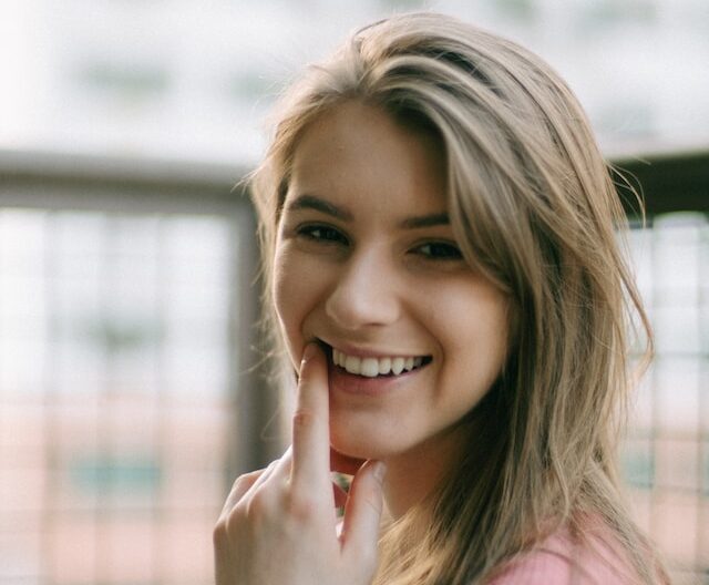 close up photo of a woman smiling and pointing at her teeth. CEREC Newport.